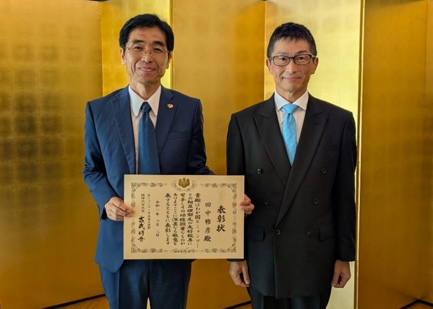 （表彰状を受け取る田中専門家（左）と、吉武臨時代理大使（右））